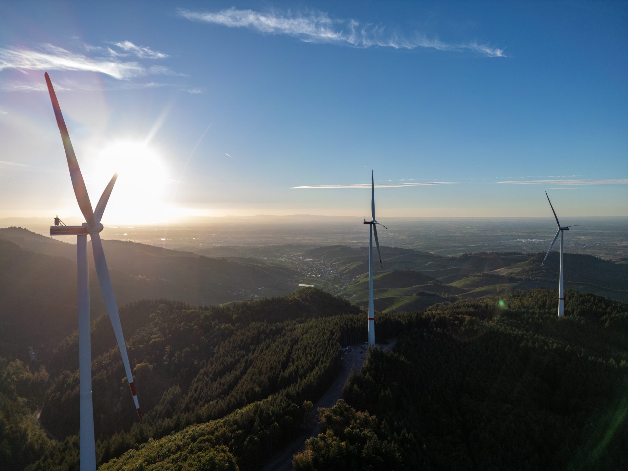 Windräder über dem Schwarzwald mit Blick auf die Rheinebene im Gegenlicht